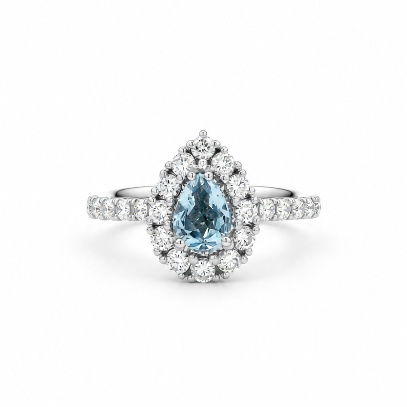 A pear-cut blue Sapphire ring with a halo of small clear stones and a diamond-like band, centered on a plain white background.