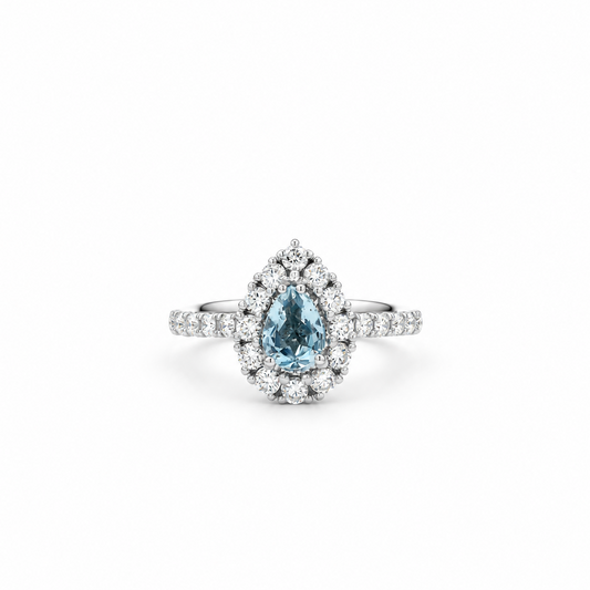 A pear-cut blue Sapphire ring with a halo of small clear stones and a diamond-like band, centered on a plain white background.
